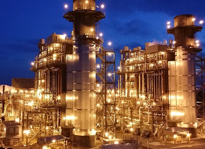 Gas turbine plant illuminated at night with exhaust stacks lit gold